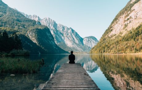 Chlapík sedí na mole a pozerá na krásne hory a rieku